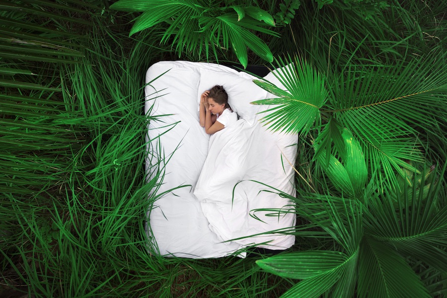 野外の緑の植物に囲まれたベッドで眠る女性